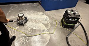 Swing machine lifting old floor finish, with stripper slurry and a wet vac staged on a commercial concrete floor